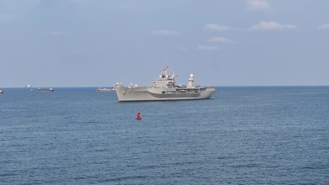 large naval amphibious assault ship being assisted by tugboats in the strategic Strait of Hormuz. Concept of maritime security, naval power projection, and protection of international shipping lanes.
