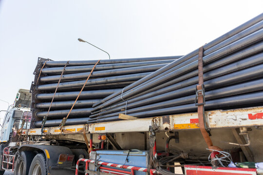 Heavy black steel pipe load on flatbed truck for industrial construction transport, showing strong sturdy feeling ready for large building project under clear daytime sky