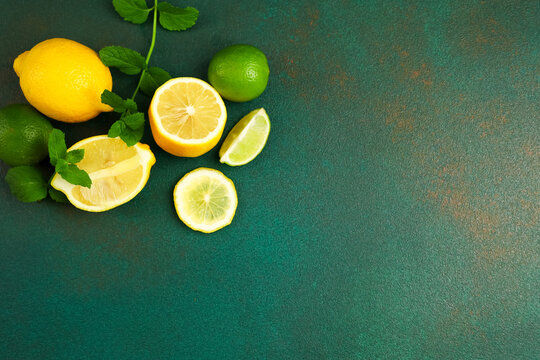Fresh lemons and limes sliced with green leaves on dark green table surface in bright light