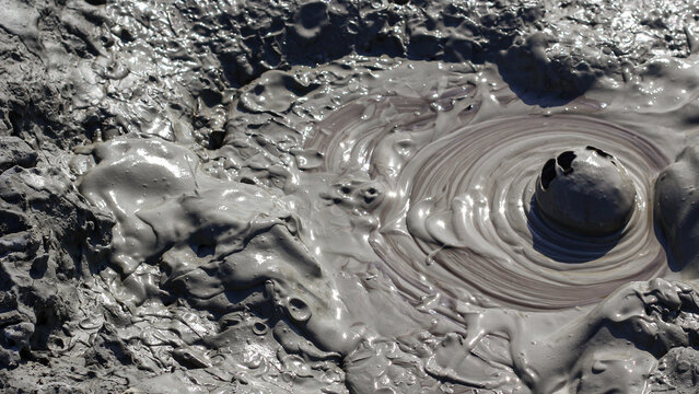 Bubbling mud volcano crater with geothermal activity and swirling clay texture