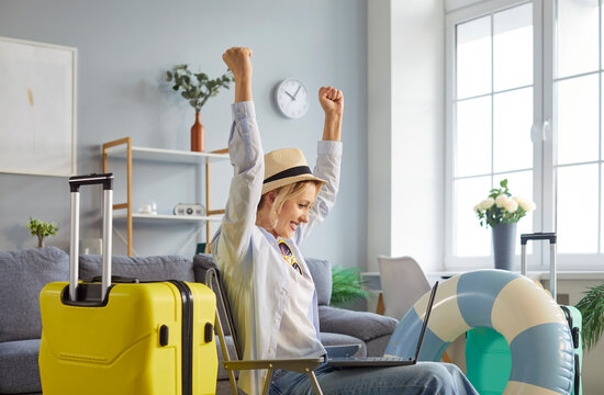 Joyful woman tourist happy to reserve travel ticket, going to spend summer vacations abroad, packed things in suitcase, focused at laptop screen and clenching fists with success. Tourism concept