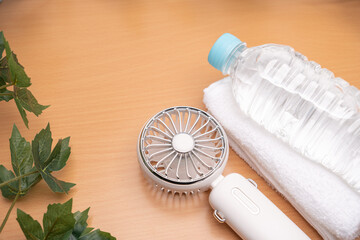 Portable handheld fan with water bottle and towel on wooden table summer cooling concept © Soft Grain Studio
