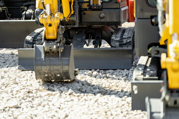 Mini excavator with black metal bucket and dozer blade resting on light grey gravel stones at a construction site, representing compact engineering and urban development © K