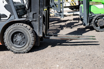 Heavy duty industrial forklift with steel forks and rugged black tires parked on a gravel surface, representing warehouse logistics and material handling efficiency © K
