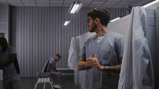 Diverse Group of Male Doctors in Surgical Scrubs and Lab Coats Interact by Grey Lockers, Hanging Up Uniforms and Preparing to Leave Hospital After Shift. Concept of Professional Medical Environment.