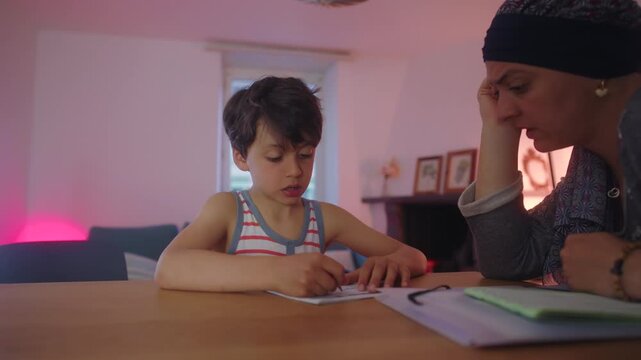 Mother helping son with homework at table in evening, focused parenting and learning support in home education routine, concentration and guidance in family study moment