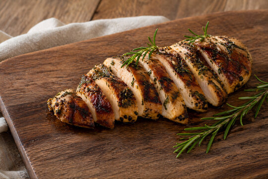 Sliced Grilled Chicken Breast with Herbs on Wooden Board