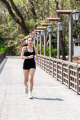 Fototapeta premium Young athletic woman jogging on park bridge while listening to music with headphones, outdoor running and healthy lifestyle fitness concept.