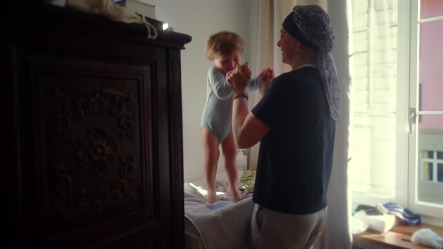 Mother dancing with baby on bed near window at home, playful parenting moment and joyful bonding during daily routine, happiness and connection in warm indoor setting