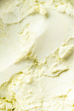 Close-up shot of creamy, pale yellow vanilla ice cream or buttercream frosting with a smooth yet textured, swirled surface.