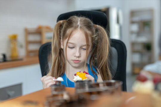 Cute little girl eating ice cream dessert in kitchen, child enjoying sweet snack with spoon, lifestyle moment, healthy happy kid concept, family indoor activity background.