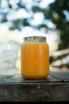 Clear plastic can filled with fresh orange juice placed on wood table background under a sunbeam
