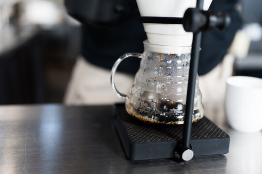 Professional barista making filtered drip coffee in coffee shop. Close up brewing a drip hot espresso, pour over coffee with hot water and filter paper in cafe.