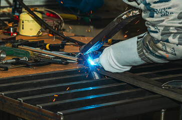 Obraz premium Welding of metal components with sparks flying in workshop. Production table with industrial tools..