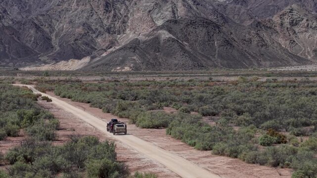 An SUV pulls a teardrop camper trailer along a dusty road in Baja California Mexico on the way to find a campsite near mountains.