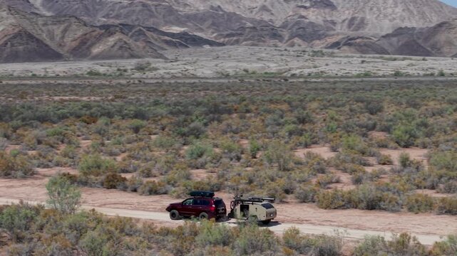 SUV pulls a teardrop camper trailer down a dusty road searching for a campsite in Baja California with mountains in the background