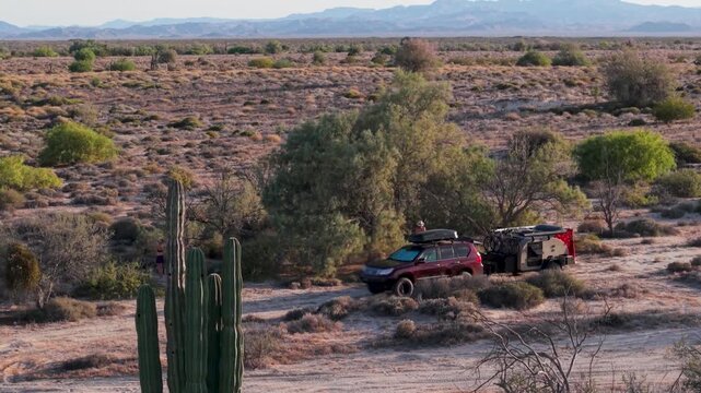 An aerial view captures an SUV with a teardrop camper trailer parked for dispersed camping in Baja California near the ocean.