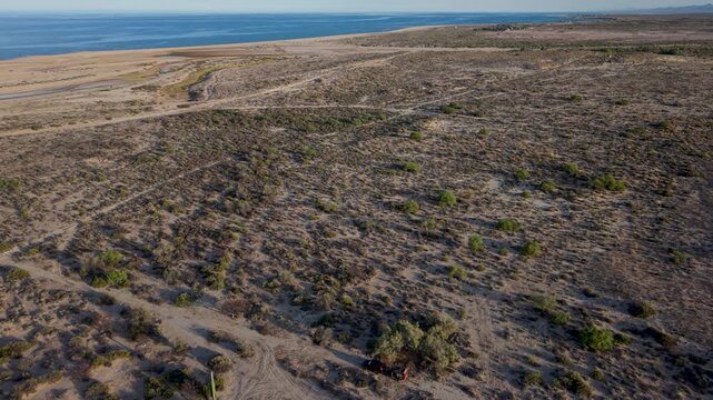 See an aerial view of an SUV with a teardrop camper at a dispersed camping spot along the Baja California coast near the ocean.