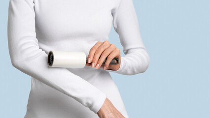 Obraz premium Woman cleaning white long sleeve with adhesive sticky roller removing lint on pastel blue background. Concept wardrobe care, slow fashion mindset, tidy fresh minimal clothing look. Copy space, banner