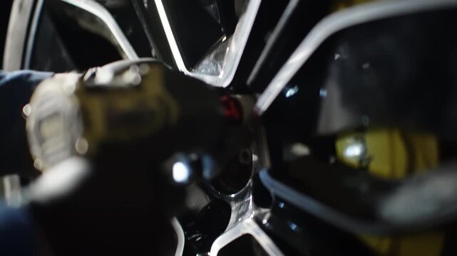 Close-up of a mechanic in gloves using an impact wrench to tighten lug nuts on a glossy alloy wheel, showing precise automotive maintenance and performance brake hardware.