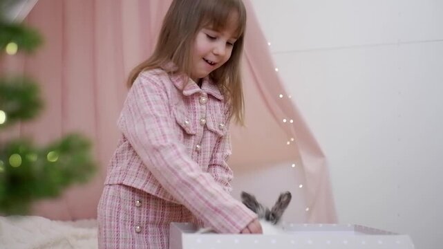 Surprised little girl opening a gift box and finding a cute live bunny for christmas morning