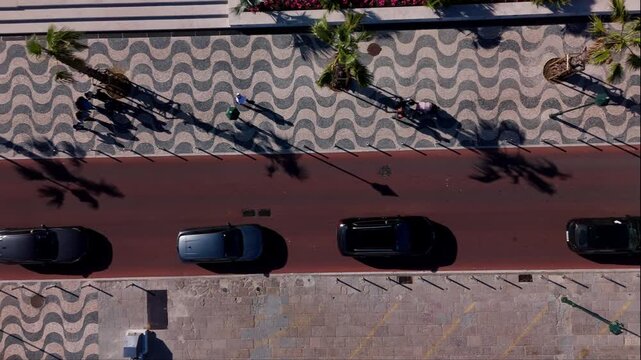 Top down aerial view of a sunny pedestrian street with tiles, alm trees and , passing cars in Cascais, Portugal
