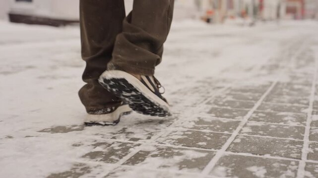 Lowangle winter walk across snowy pavement, confident stride of urban commuter, sneaker tread kicking up powder, wide city avenue, brisk tempo, clear sole pattern and resilient motion