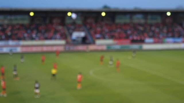 Cinematic blurred background of a football match in progress, out-of-focus players running on a green pitch, generic sports concept with copy space