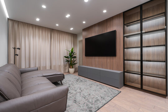 Modern living room interior with wooden accent wall, wall mounted TV, minimalist furniture and soft lighting, contemporary apartment design with neutral tones and elegant decor.