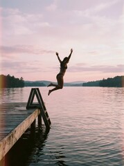 Fototapeta premium Woman Jumping from Wooden Dock into Serene Lake at Sunset