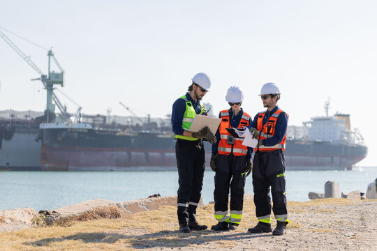 Workers discuss plans at a port with a cargo ship in the background