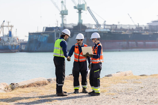 Workers discuss plans at a port with a cargo ship in the background