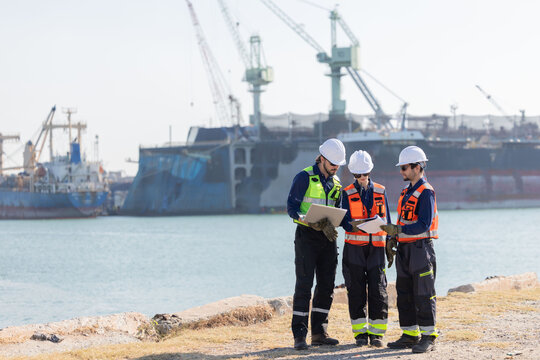 Workers discuss plans at a port with a cargo ship in the background