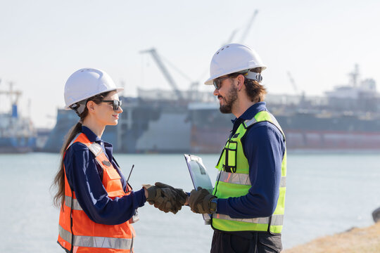 Workers shake hands at a dock area with ships and cranes in the background