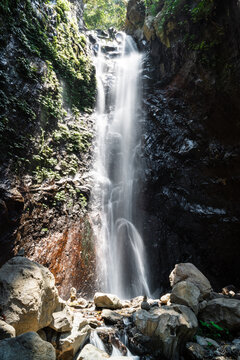 Tropical waterfall cascading over dark rocks with sunlight and mist creating a natural scene