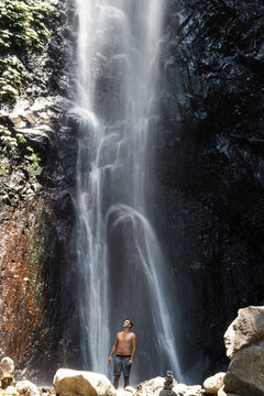 Man standing under waterfall in jungle canyon, enjoying nature in Bali