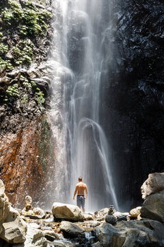 Man under powerful waterfall in jungle canyon, enjoying nature and adventure travel in Bali