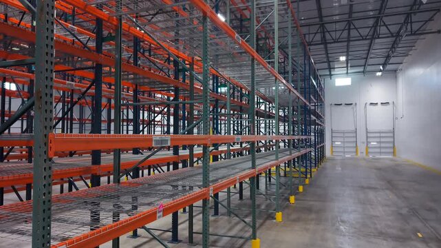 Empty Warehouse Interior with Tall Orange and Blue Shelving Racks, and closed loading dock doors