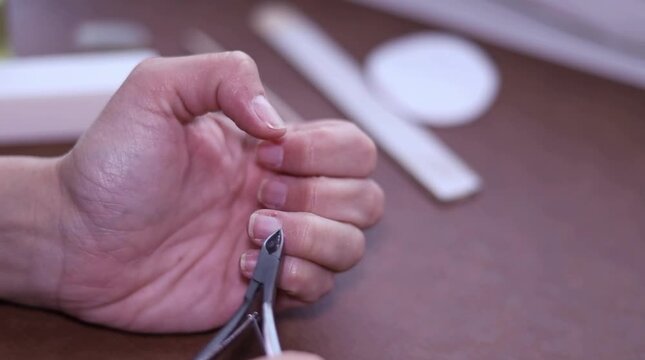Detailed close-up of a hand trimming a thumb cuticle with nippers during an indoor manicure, static