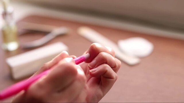 Hands pushing back cuticles with a pink tool during a home manicure, close-up, static shot.