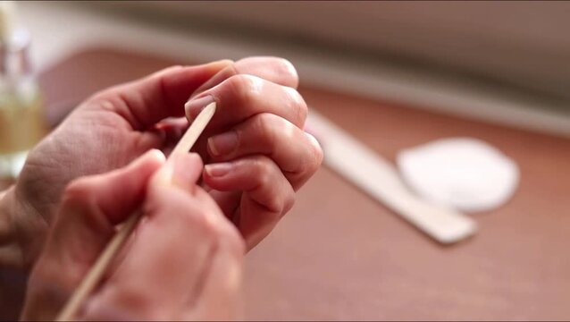 Female hands push back cuticles with a wooden stick during a home manicure routine, close-up,