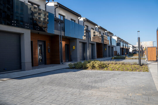 Modern row of townhouses with stylish facades and glass balconies in a clean residential neighborhood under clear blue sky.