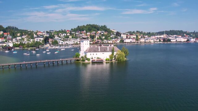 Aerial of beautiful white castle Ort Seeschloss in the Lake Traunsee, at Gmunden town. Serene lake, vibrant boats, and picturesque buildings along the shoreline. Austria tourism and scenic places