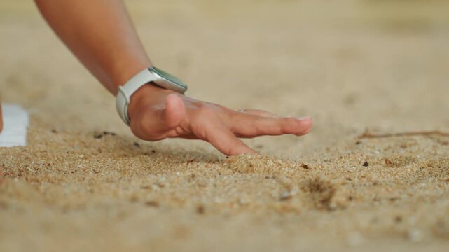 Closeup hands touching warm sand woman wearing watch and bracelet gently explores grainy beach surface with slow tactile motions sunlit texture meditative grounding exercise intimate macro detail