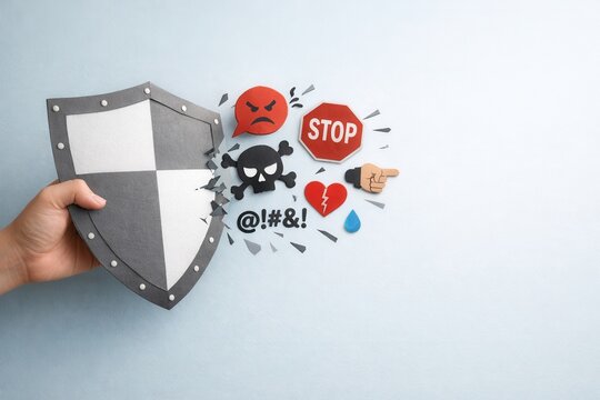 A hand holds a shield blocking negative icons like anger, stop signs, skull, and broken heart, symbolizing protection from harmful emotions and negativity.