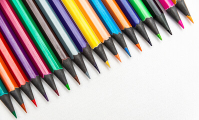 Fototapeta premium Colorful pencils arranged in a straight line on a white background during a daylight setting