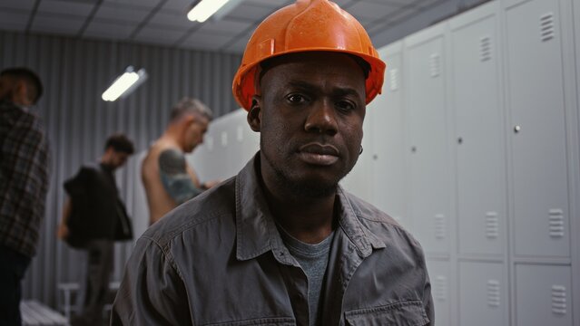 Portrait of Dedicated African American Male Worker in Orange Hard Hat, Looking Confidently Into Camera With Serious and Responsible Expression in Dressing Area. Professionalism in Heavy Industry.