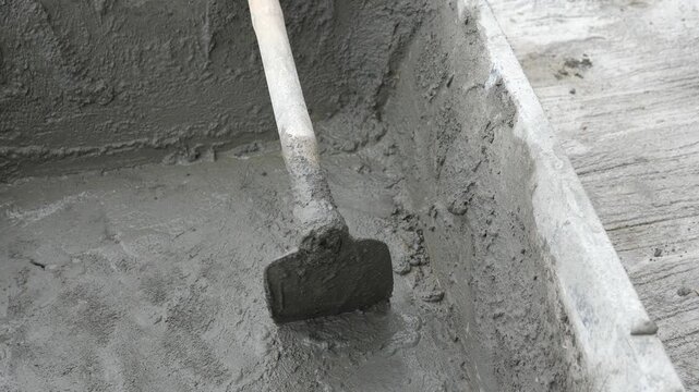 Close-up of freshly mixed wet cement in a black plastic tub with a hoe, DIY home improvement and manual labor construction concept
