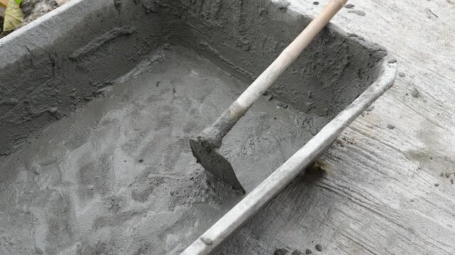 Close-up of freshly mixed wet cement in a black plastic tub with a hoe, DIY home improvement and manual labor construction concept