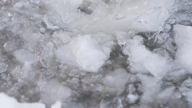 Broken ice pieces and snowy frozen fragments float inside a winter ice hole, creating a close view of rough cold texture, dark water, and scattered icy debris. High quality 4k footage